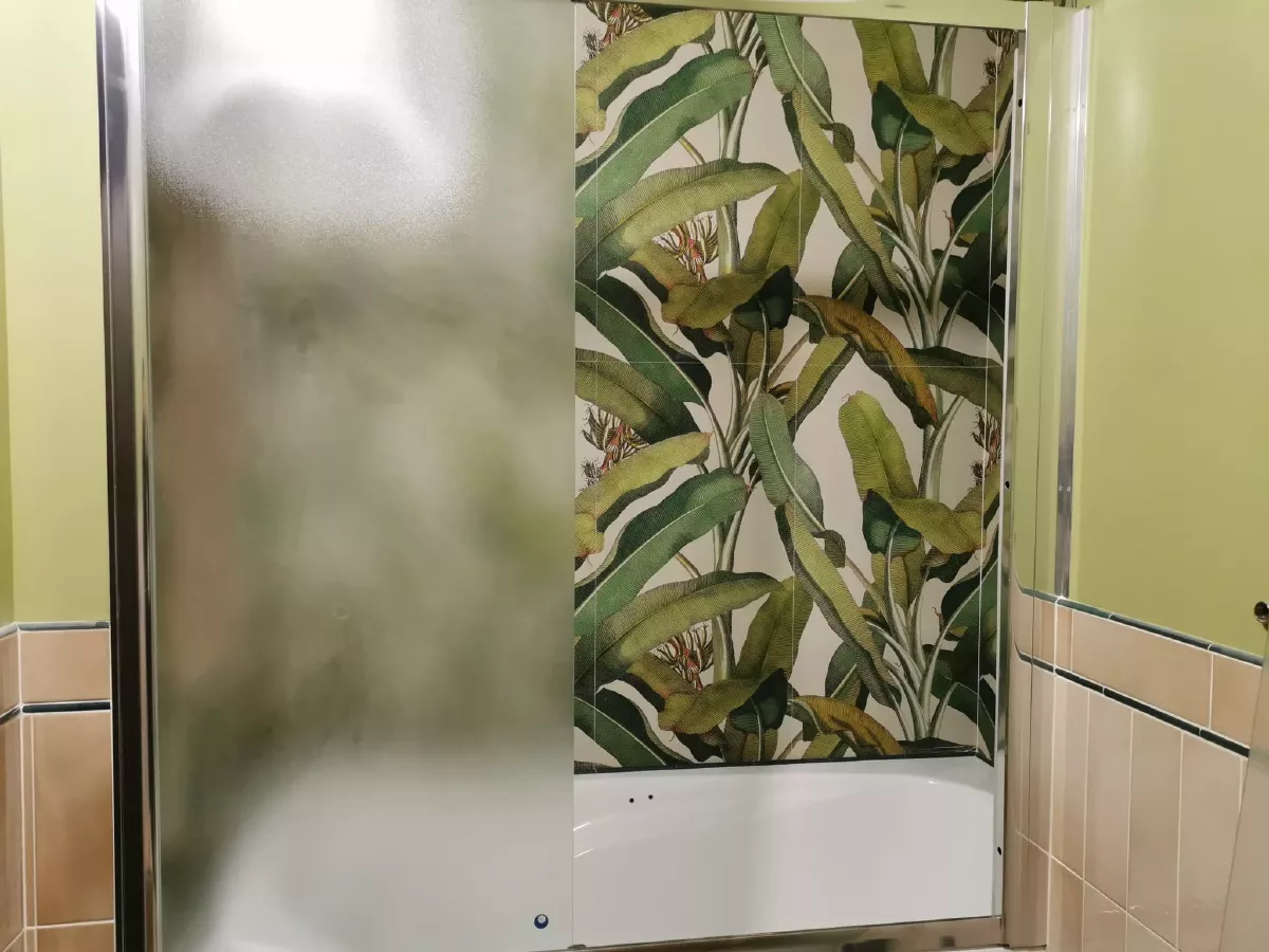 Дизайнерский ремонт ванной комнаты в новостройке: ванна в нише со стеклянной перегородкой, акцентная стена из керамогранита с тропическим растительным принтом, бежевая облицовка, чистовая отделка