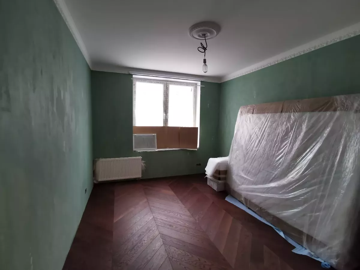 Дизайнерская отделка комнаты в новостройке: стены с декоративной штукатуркой зеленого цвета, паркет французская елка, белые гипсовые молдинги и потолочная розетка, мебель в защитной пленке