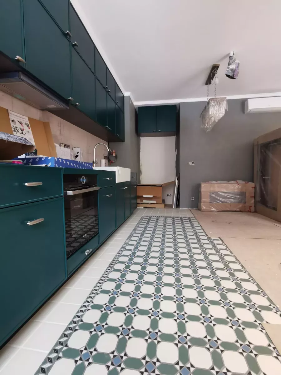 Дизайнерский ремонт кухни в новостройке: темно-зеленые кухонные фасады, геометрическая плитка на полу, серые стены с декоративной штукатуркой, гипсокартонный потолок с гипсовыми плинтусами, хрустальная люстра и кондиционер